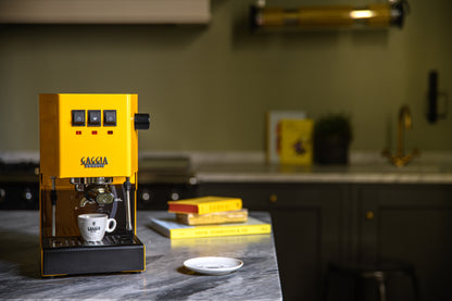 Gaggia Classic E24 espressomaskin gul på bänk med espressokopp, och böcker